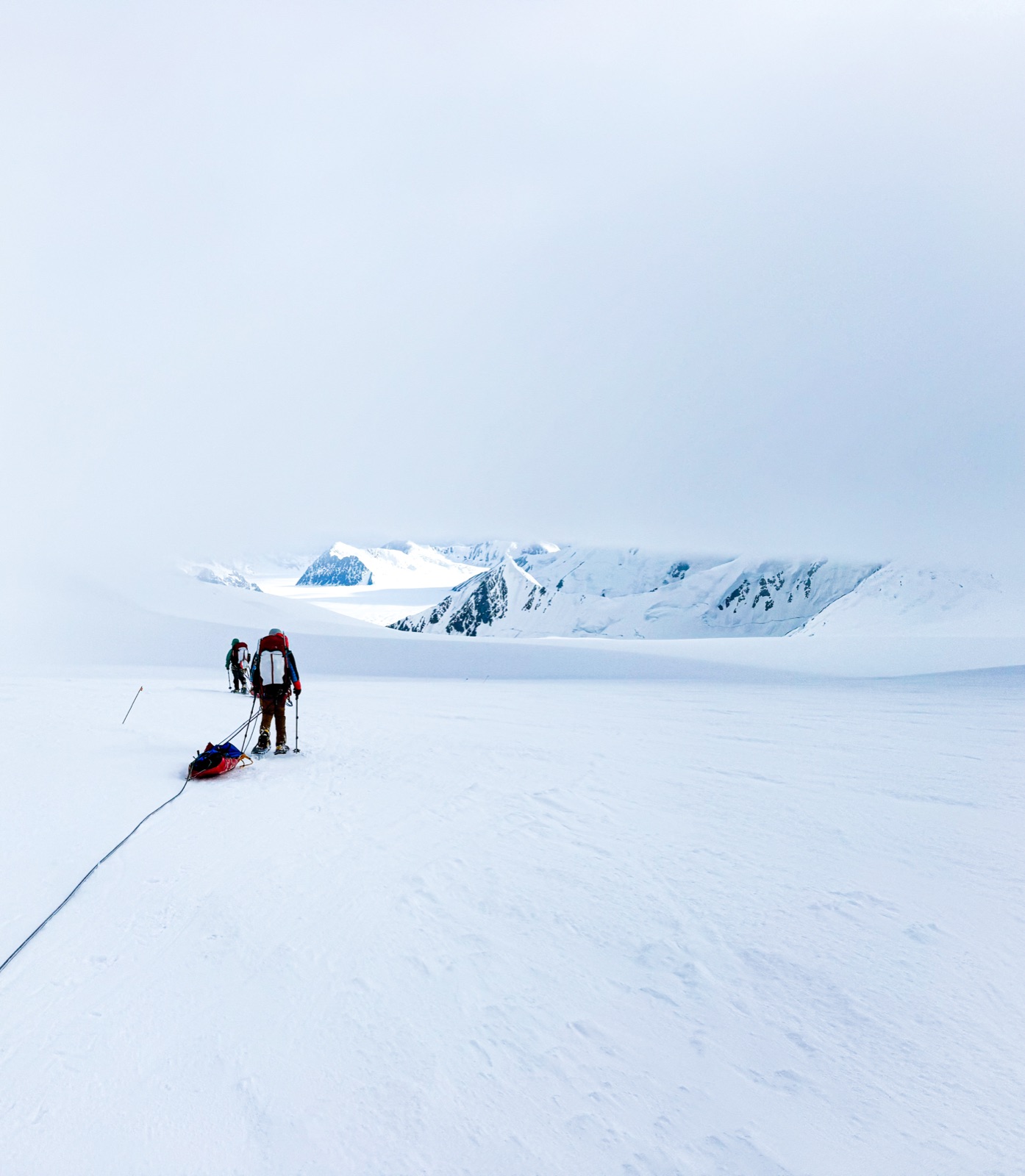A climber pulling a sled across a wide, white glacier