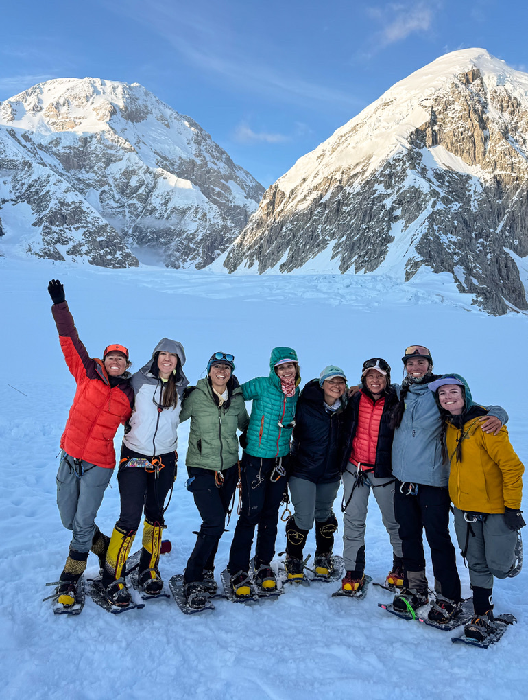An all-women rope team on snowshoes on the Kahiltna Glacier, with Denali's peaks behind them